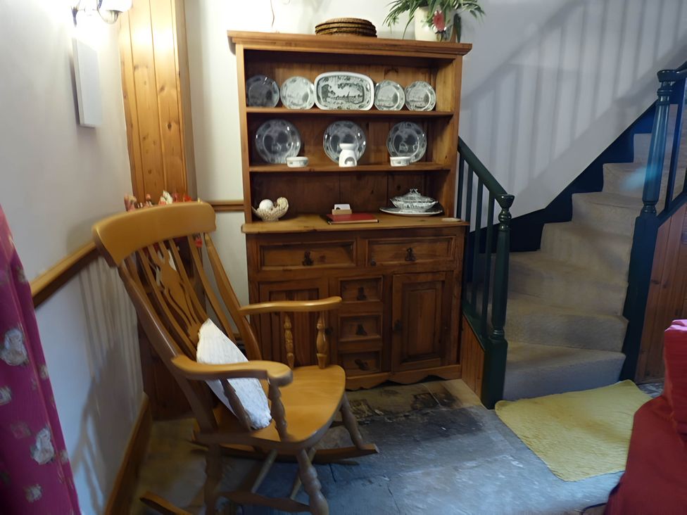 A living room with a rocking chair and a shelf of dishes at Quiet cottage on the rural edge of Brixham