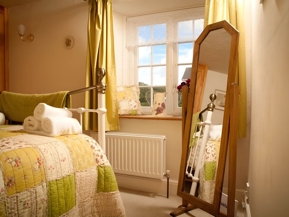 A bedroom with a bed, towels, mirror and window at Quiet cottage on the rural edge of Brixham