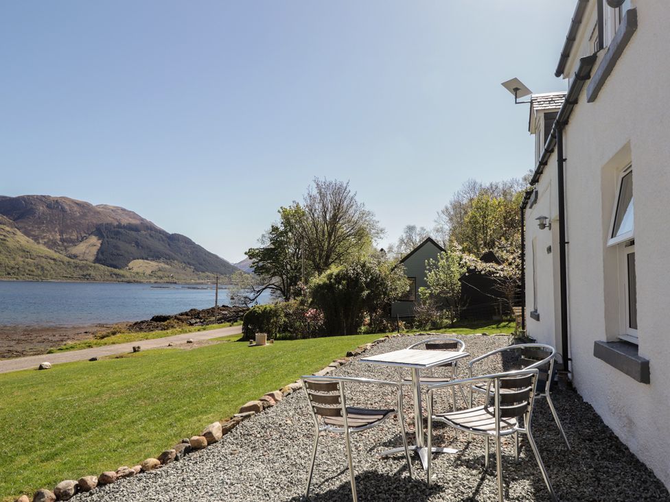 A patio with a table and chairs facing a lake and mountains at Tigh a Phailean in Letterfearn