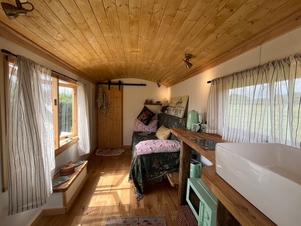 A living room with a sofa and kitchenette at Shepherd Hut in Gloucester