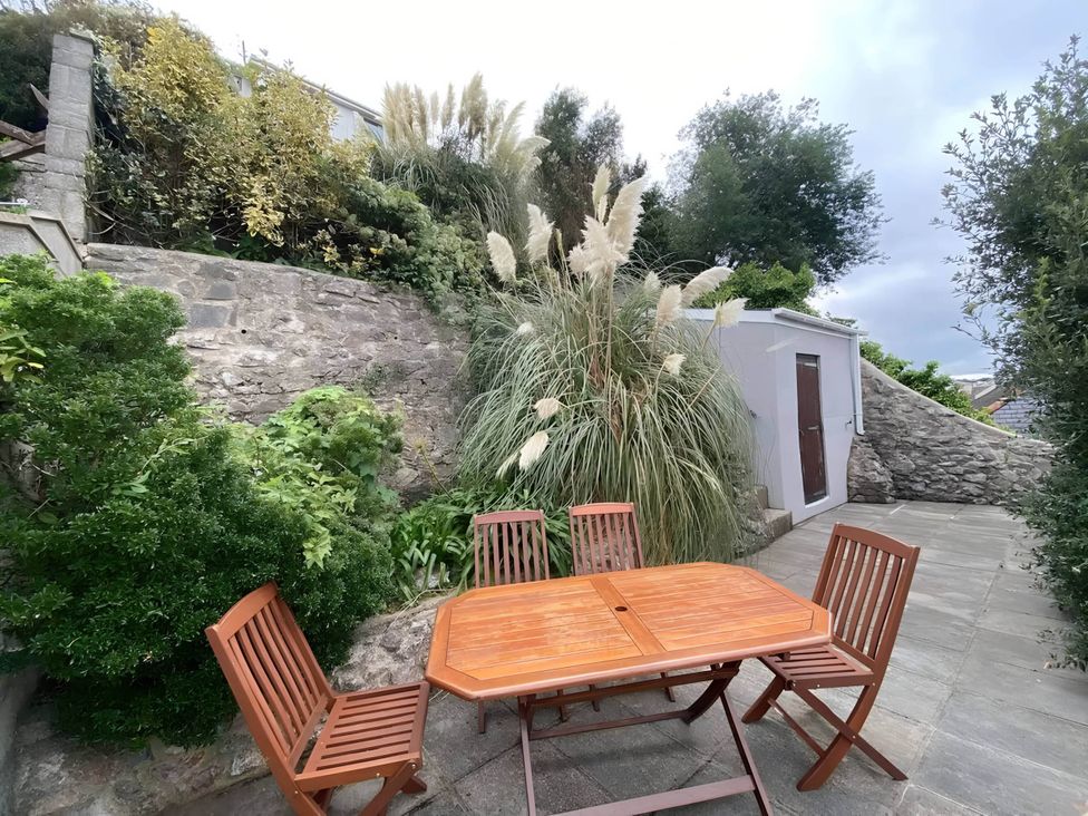 A garden with a wooden table and chairs surrounded by plants at 4 Bed House-Sleeps 8-Parking-Pets-MarinaSeaView in Torquay