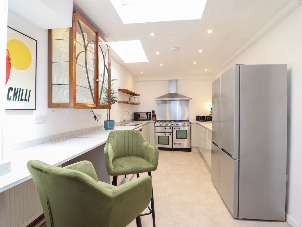 A kitchen with a refrigerator, oven, sink, and bar stools at Sea View, East Parade Llandudno