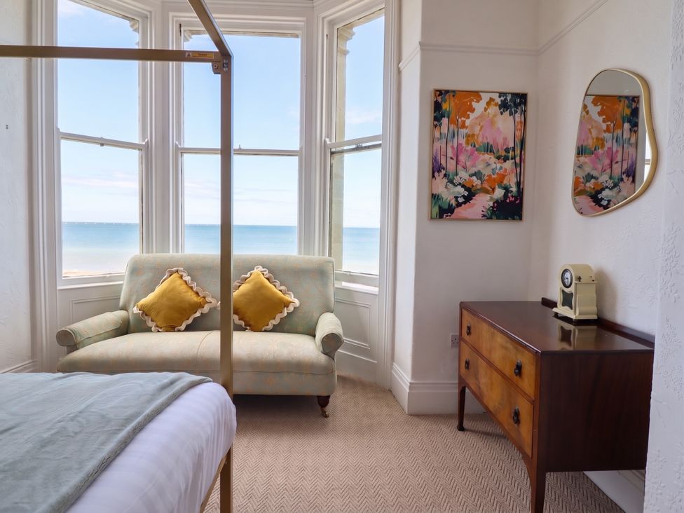 A bedroom with a sofa, dresser, and window view at Sea View, East Parade in Llandudno