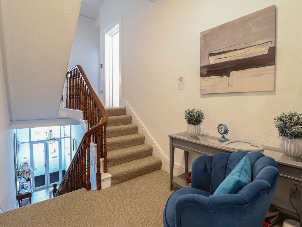 A hallway with a staircase and a chair at Sea View, East Parade, Llandudno