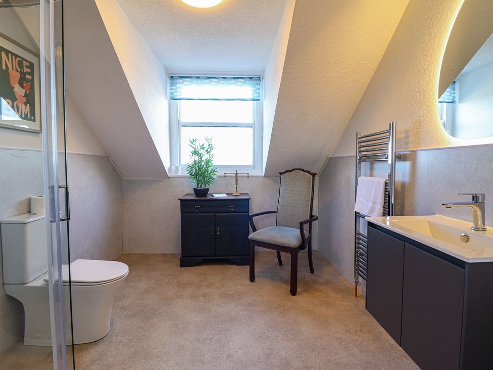 A bathroom with a sink, toilet, and a chair at Sea View, East Parade in Llandudno