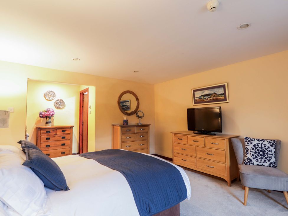 A bedroom with a bed, dresser, television and armchair at Dunhallin House in Inverness