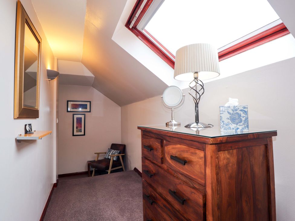 A hallway with a dresser, lamp, and chair at Dunhallin House in Inverness