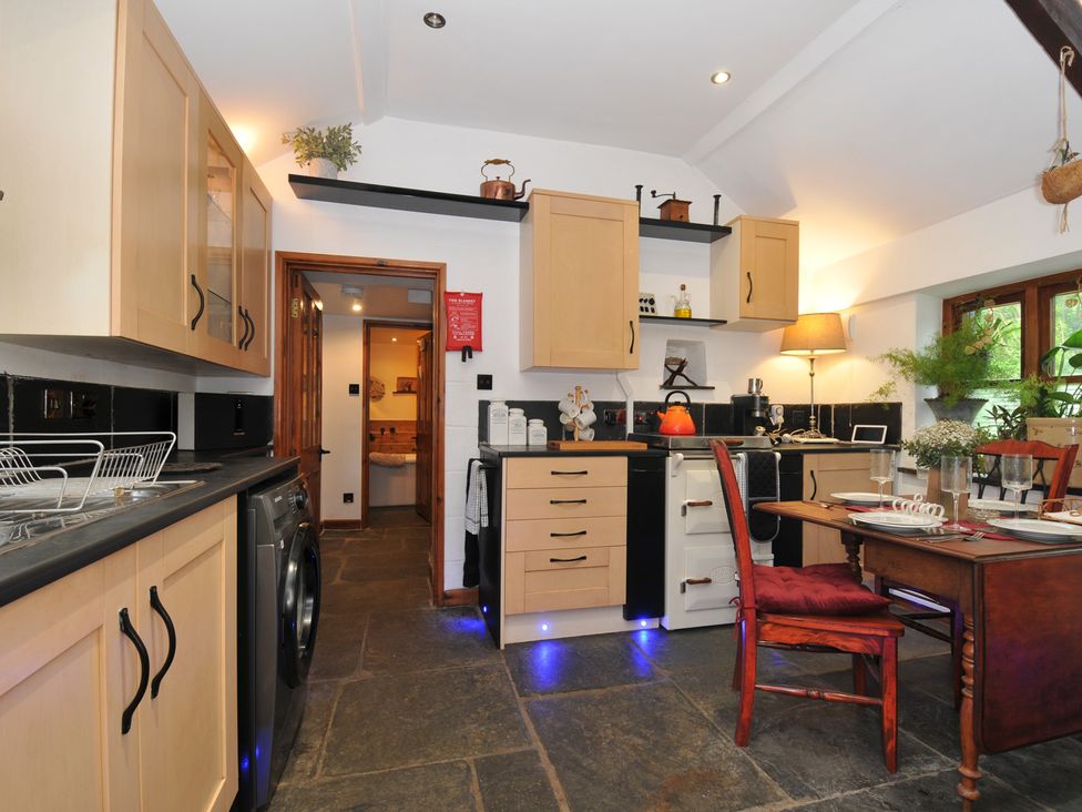 A kitchen with cabinets, a table and chair at Coach House in Camelford