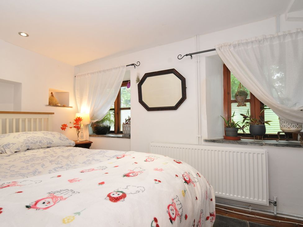 A bedroom with a bed, bedside table, lamp and windows at Coach House in Camelford