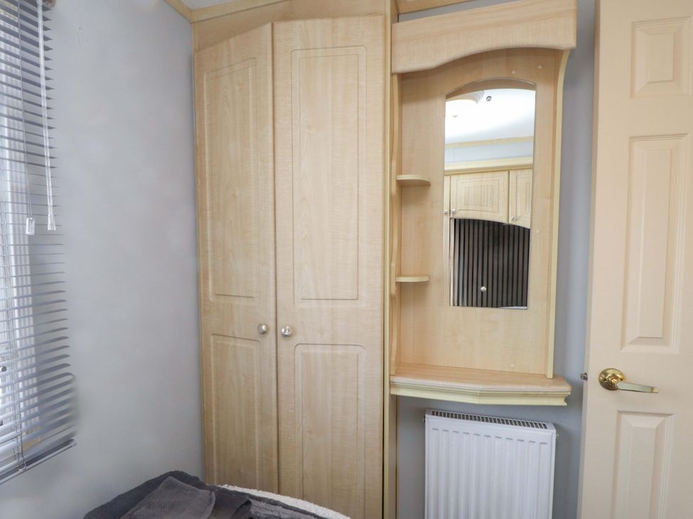 A bedroom with a wardrobe and mirror at Caravan at Argraig near Cemaes Bay