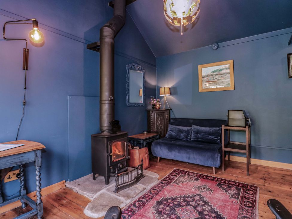 A sitting room with a stove, sofa, coffee table, and artwork at Ferryman's Lodge in Brockweir