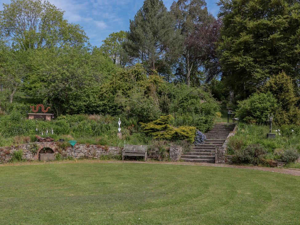 A garden with grass, a bench, stairs, trees, and sculptures at Ferryman's Lodge in Brockweir