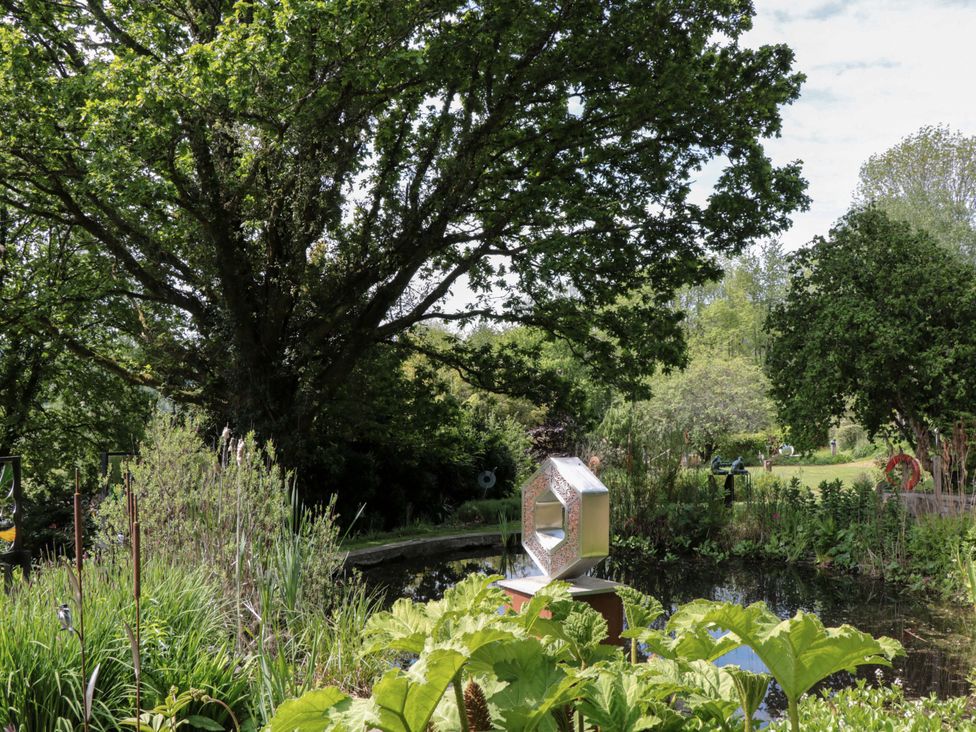 A garden with a pond, sculpture, and large trees at Ferryman's Lodge in Brockweir