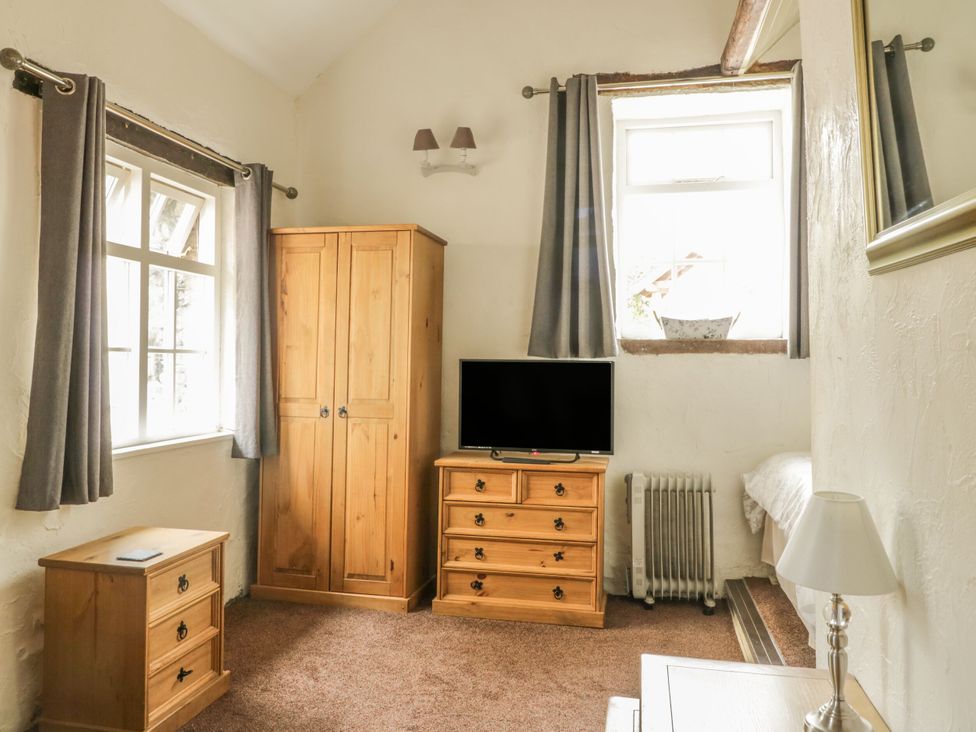 A bedroom with furniture including a wardrobe, TV, and chest of drawers at Mews Cottage 7 in Braithwaite