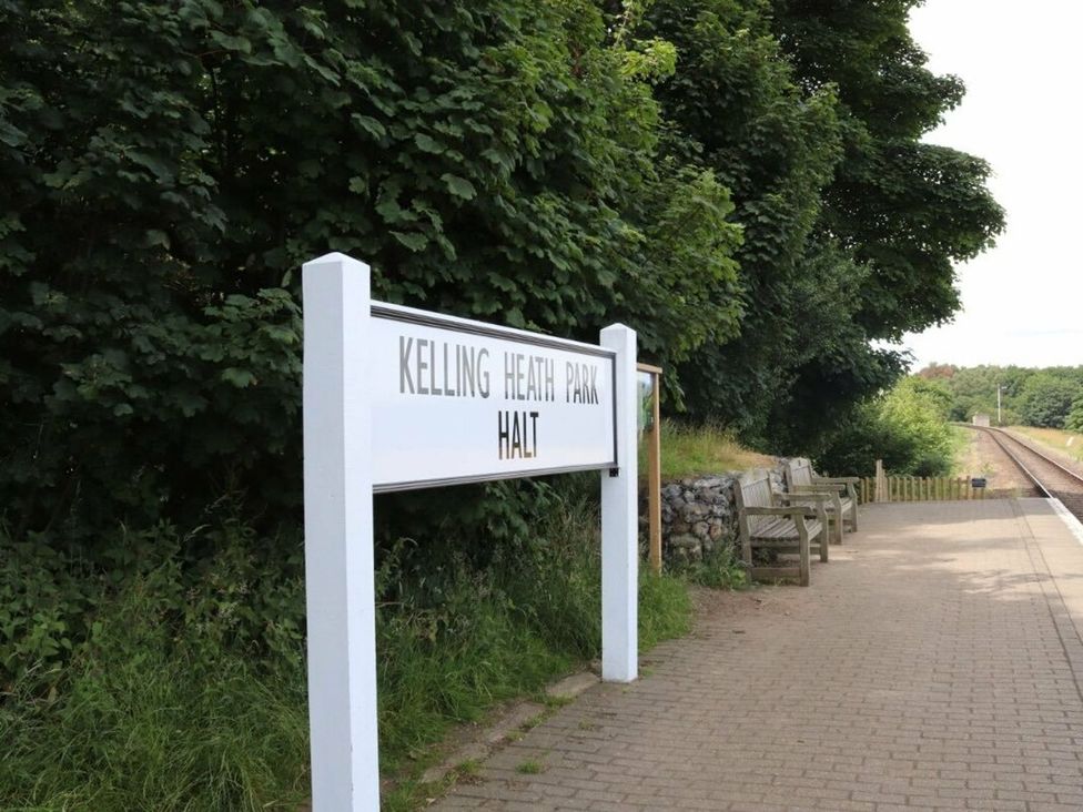 A sign for Kelling Heath Park Halt with benches and a railway in the background