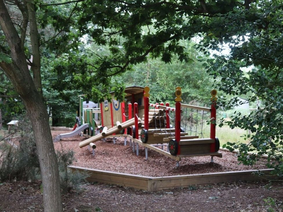 Playground with slide and climbing frame in a wooded area at Living The Dream in Holt