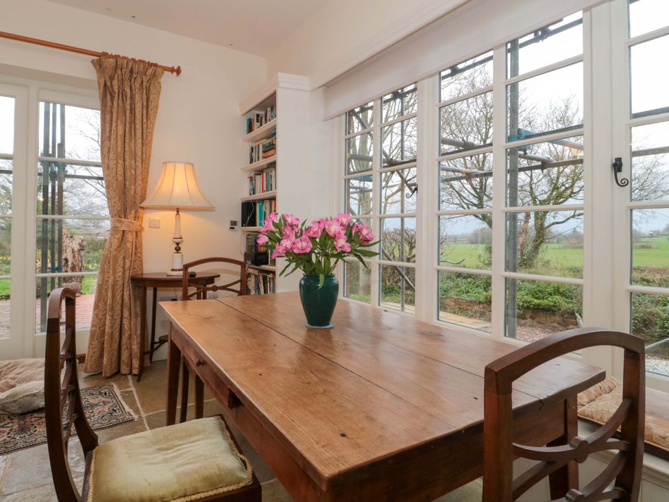 A dining room with a wooden table and flowers at Tuxwell Lodge in Spaxton near Nether Stowey