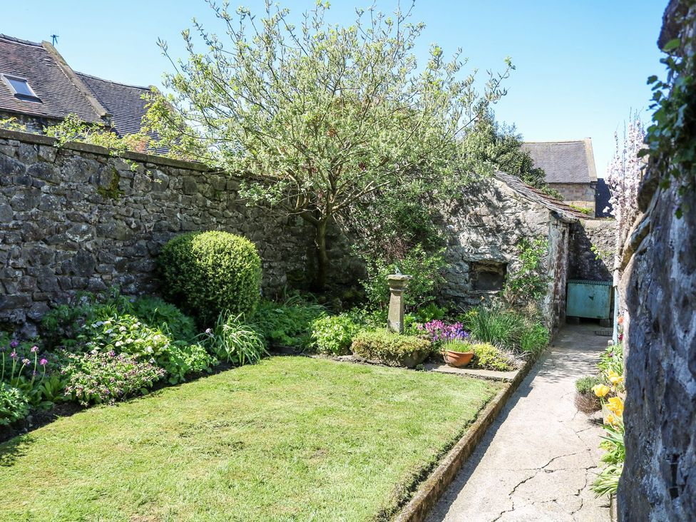 A garden with a stone wall and plants at Ivy Cottage in Hartington