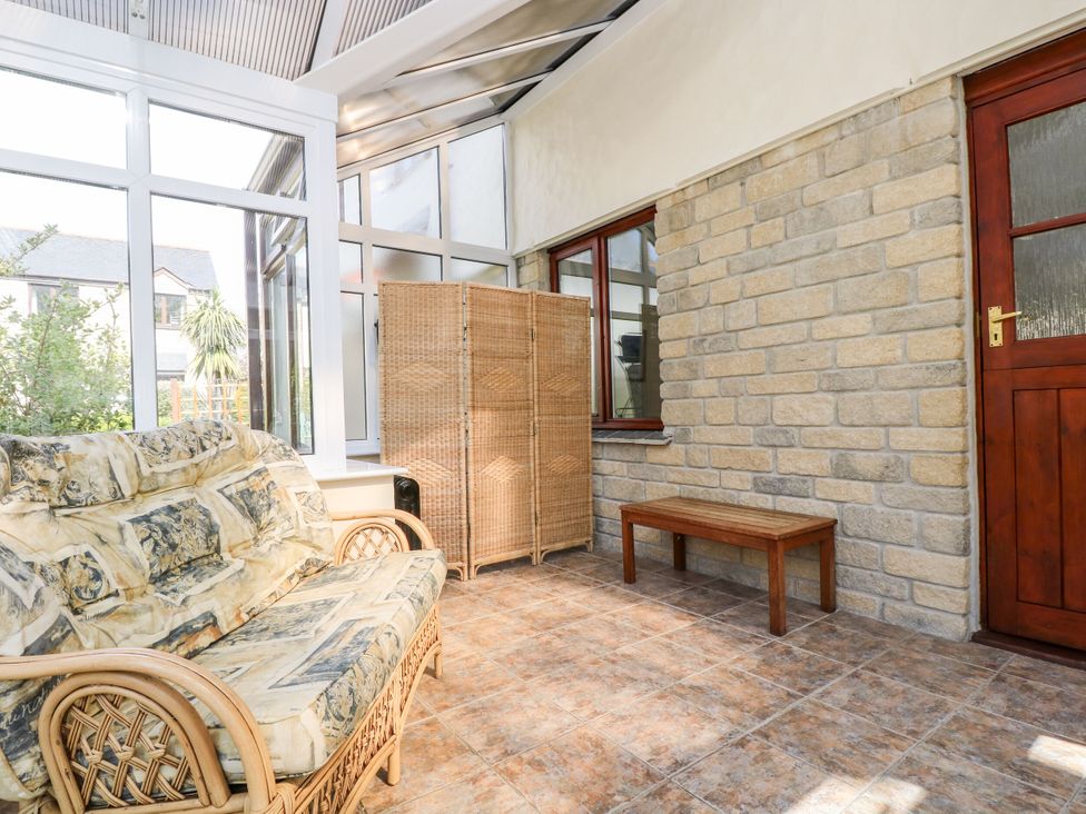 A conservatory with a sofa and wooden table at Oak Cottage in Falmouth