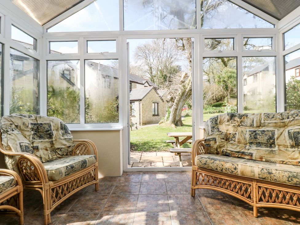 A conservatory with wicker sofas looking out to the garden at Oak Cottage in Falmouth