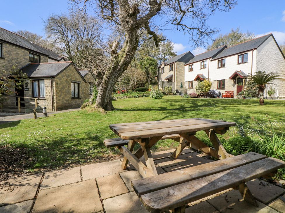 A garden with a wooden picnic table surrounded by trees and two houses at Oak Cottage in Falmouth