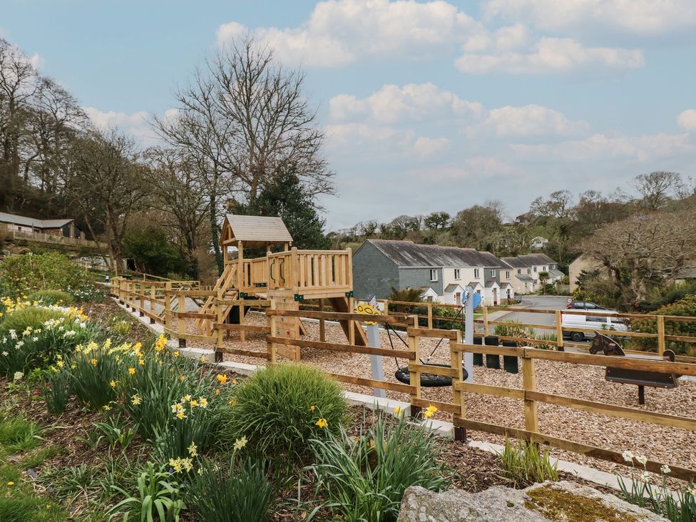 A playground with a playhouse and swings at Oak Cottage in Falmouth