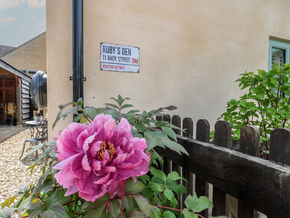 A sign for Ruby's Den with a flower in the foreground at Ruby’s Den Ashton Keynes