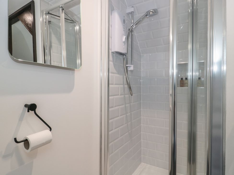 A shower with a mirror and toilet paper holder at Ruby’s Den Ashton Keynes