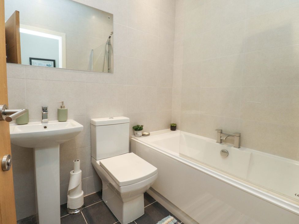 A bathroom with a bath tub, toilet, sink, and mirror at Flat 2, Dorstan in Carnforth