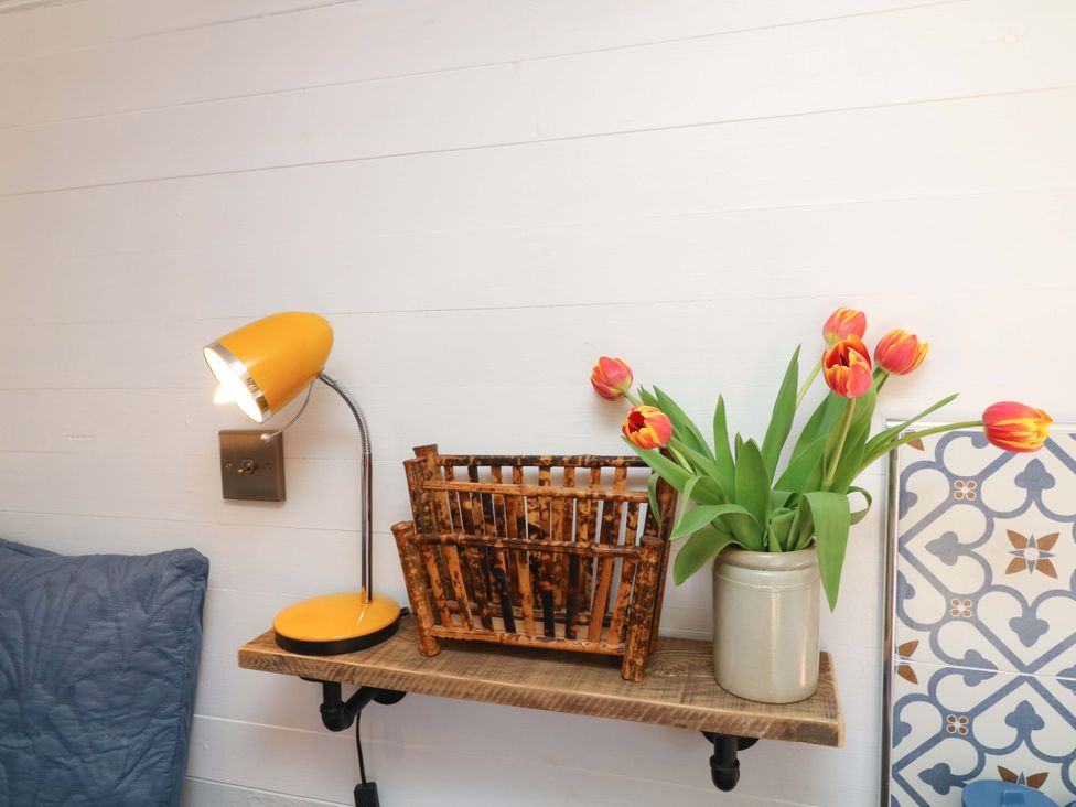 A living room with a lamp and flowers on a shelf at Shepherds Hut in South Hykeham