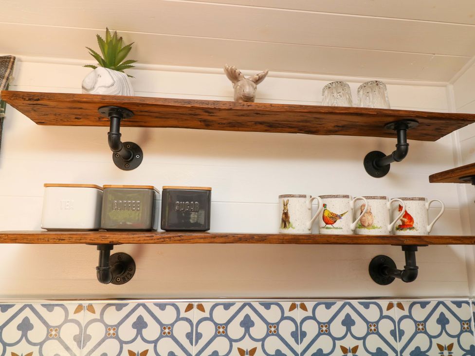 A kitchen with shelves holding jars and mugs at Shepherds Hut South Hykeham