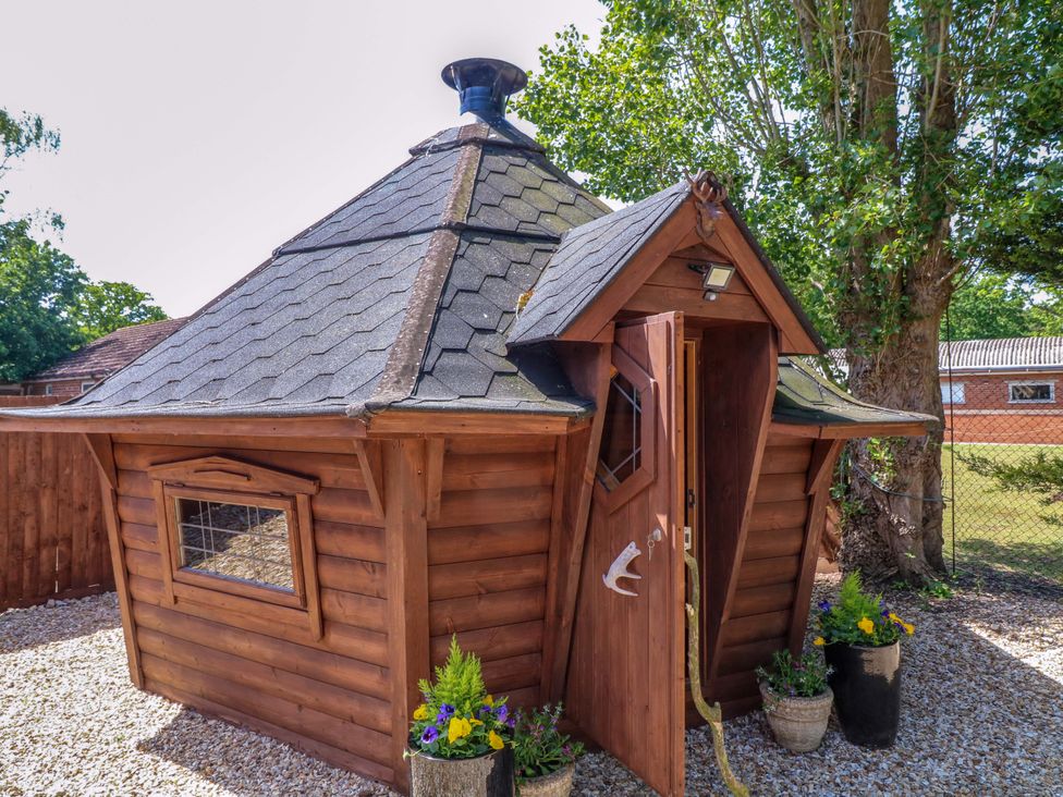 A wooden hut with a triangular roof and door at Shepherds Hut South Hykeham