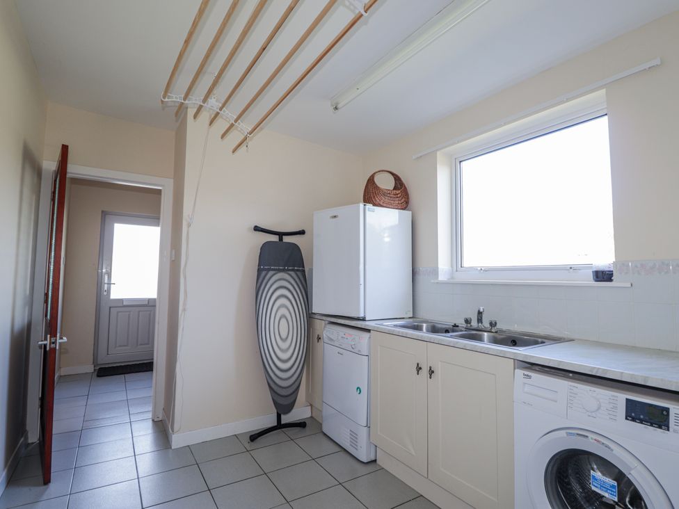 A utility room with a fridge, washing machine, and sink at An Grianan in Kinlochbervie
