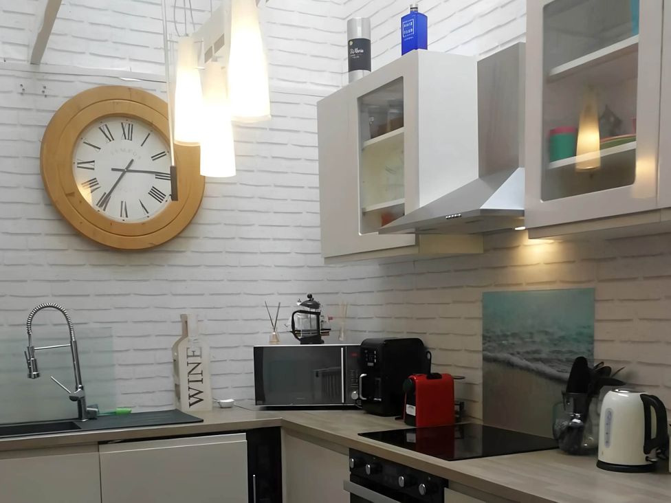 A kitchen with a clock, sink, microwave, coffee maker, and wine bottle at House - Sleeps 7 - Garden - Pets Ok - Parking in Torquay