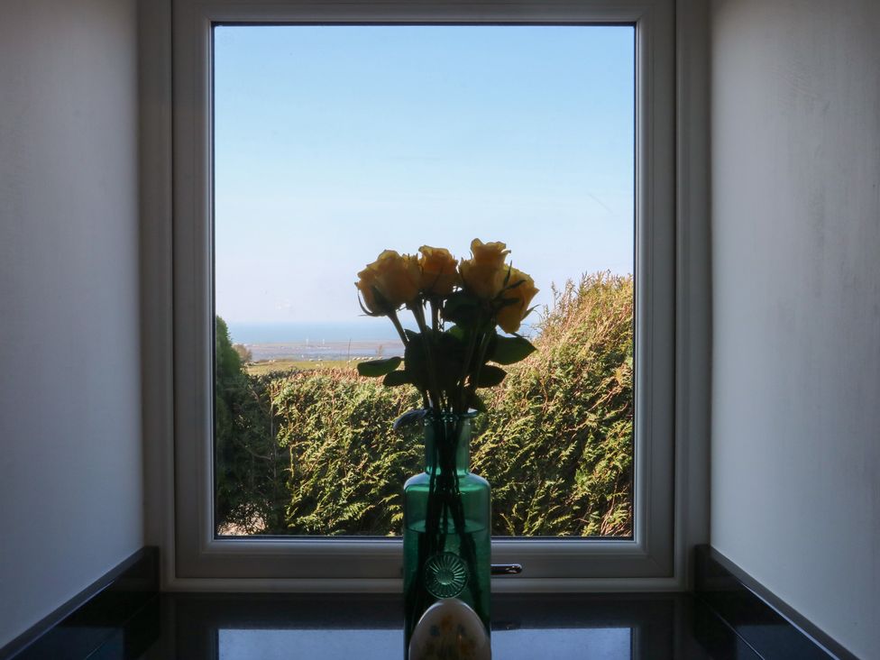 A window with a vase of flowers and a view of bushes and the sea at Studio near Bontnewydd