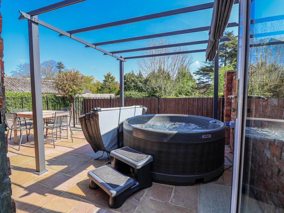 An outdoor patio with a hot tub and dining table at Elwy Cottage St Asaph