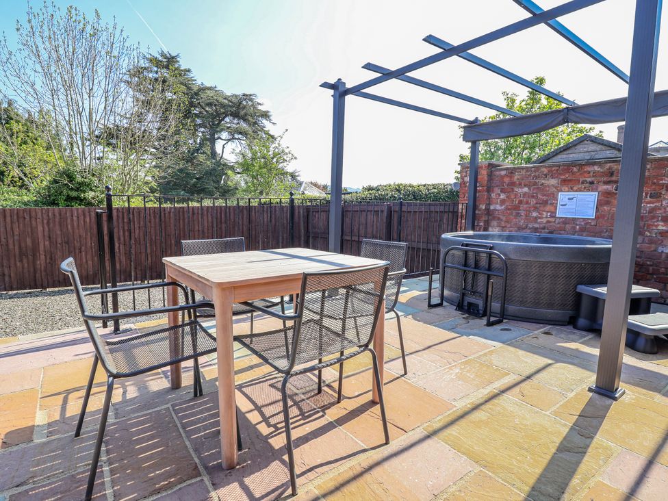 An outdoor area with a table, chairs, and a hot tub at Elwy Cottage in St Asaph