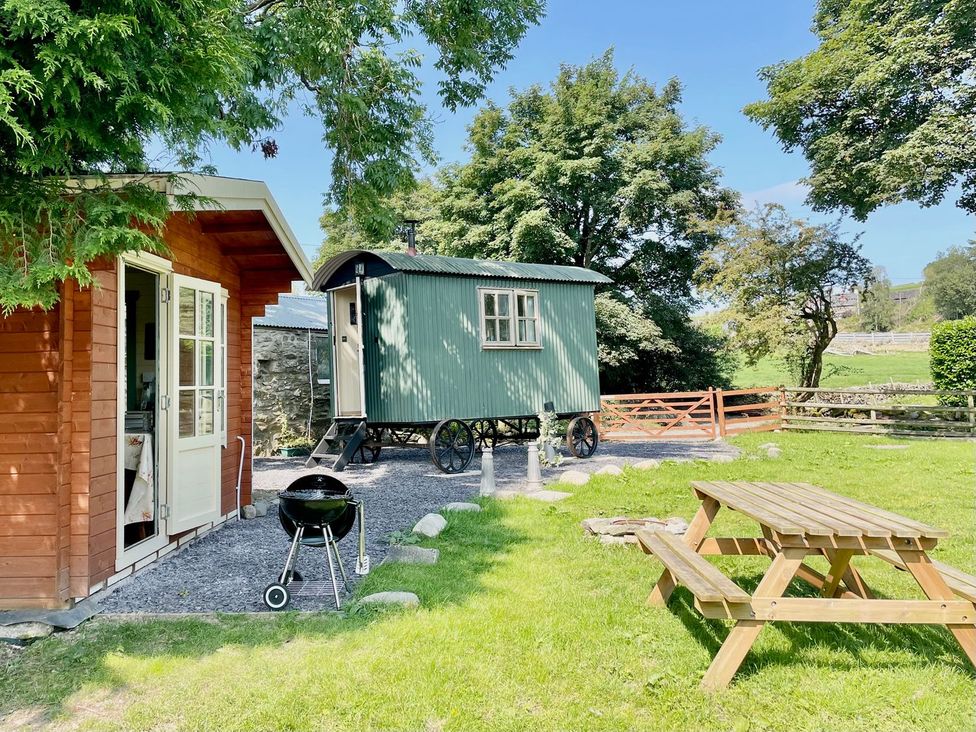 An outdoor space with a hut, grill, and picnic table at Cwt Tyddyn Shepherd's Hut in Corwen