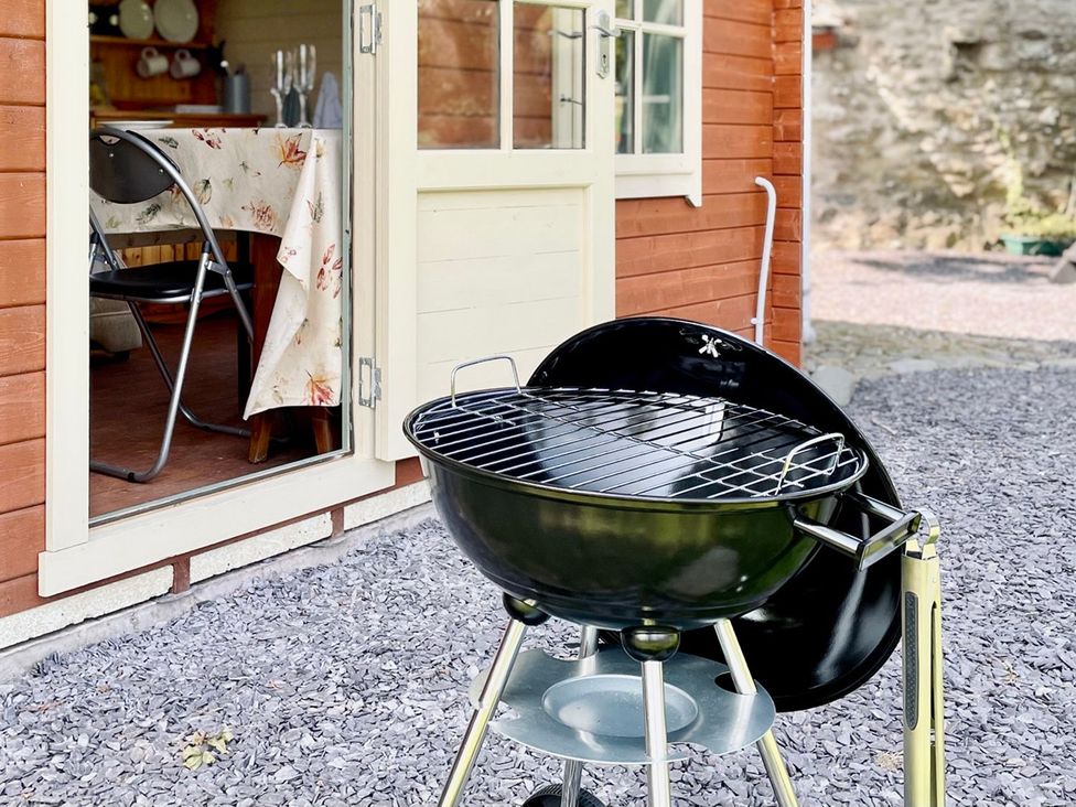 A grill with a table and chair at Cwt Tyddyn Shepherd's Hut in Corwen