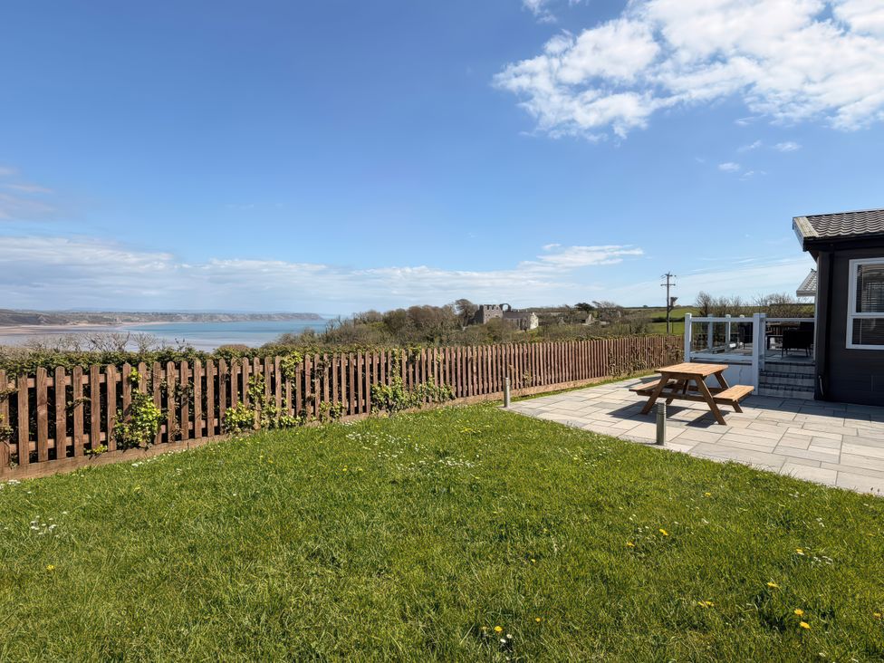 A garden with a table and chairs overlooking the water at Wernlas Lodge in Oxwich
