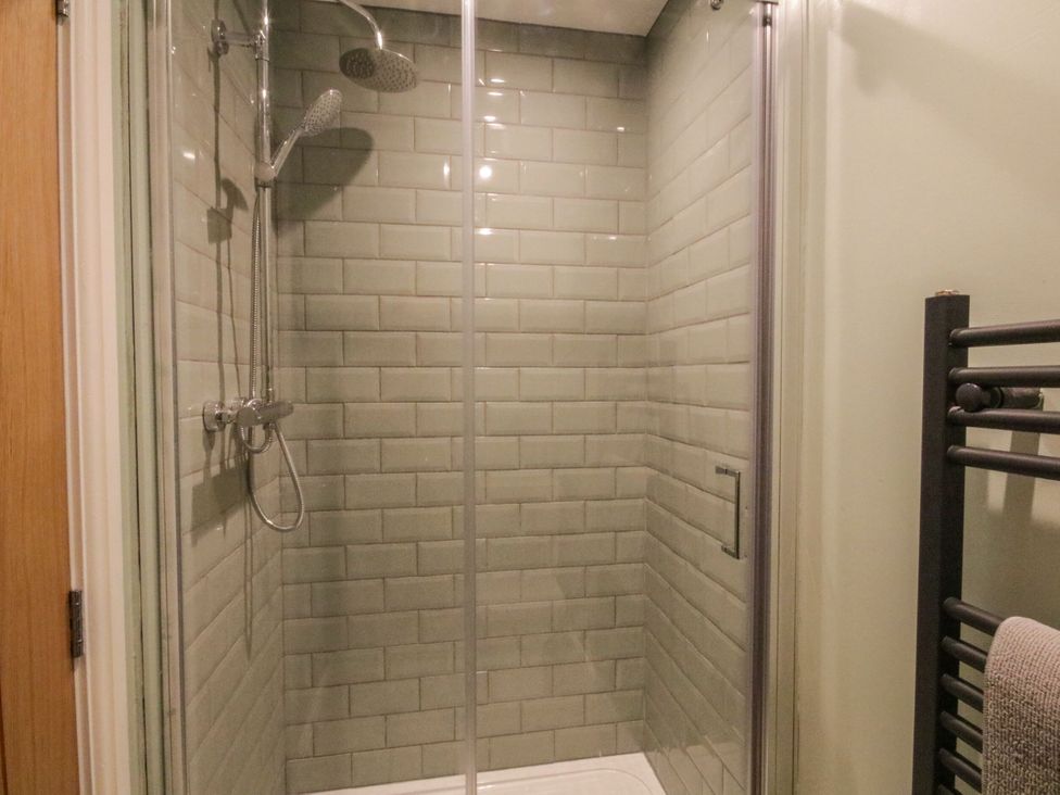 A shower with glass door and tiled wall at Sun Trevor Barns 2 Llangollen