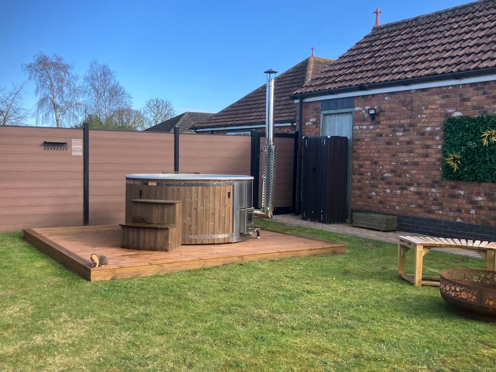 A hot tub on a wooden deck in a garden at Twit Twoo Shepherds Hut North Somercotes
