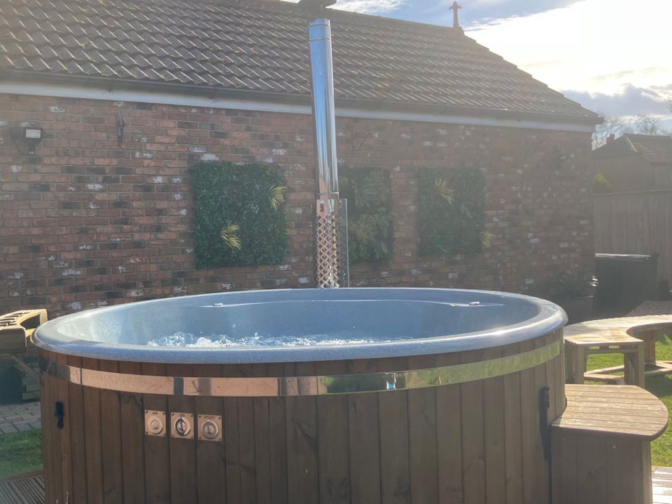 A hot tub with wooden surround in a garden at Twit Twoo Shepherds Hut North Somercotes