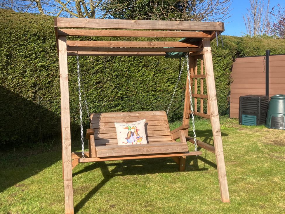 A swing seat with chains and a cushion in a garden at Twit Twoo Shepherds Hut North Somercotes