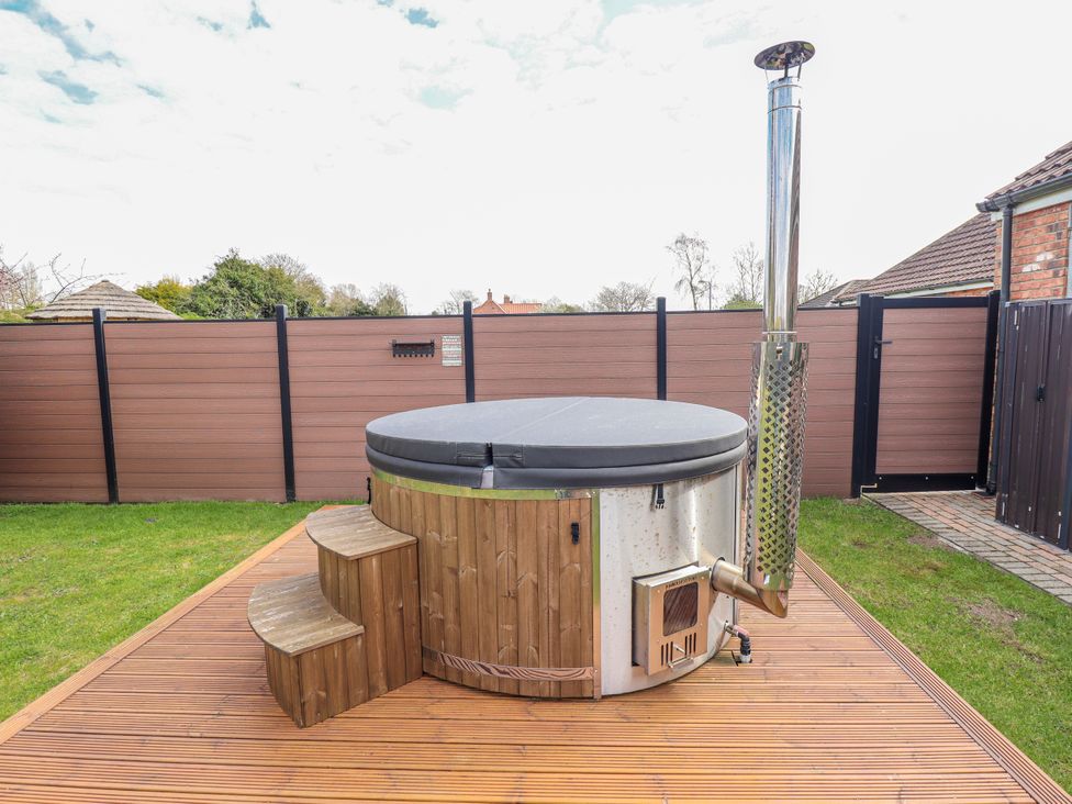 A hot tub with steps and a smokestack in a garden at Twit Twoo Shepherds Hut North Somercotes