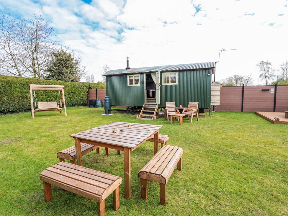 A garden with a shepherd hut, table and benches at Twit Twoo Shepherds Hut North Somercotes