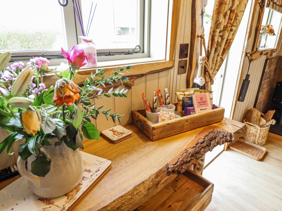 A kitchen area featuring a wooden table with flowers and snacks at Twit Twoo Shepherds Hut North Somercotes