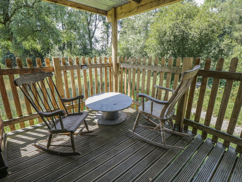 An outdoor seating area with rocking chairs and a table at Owls Nest Lodge in South Molton