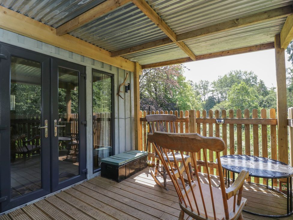 A wooden deck area with a rocking chair and table at Robins Nest Lodge in South Molton