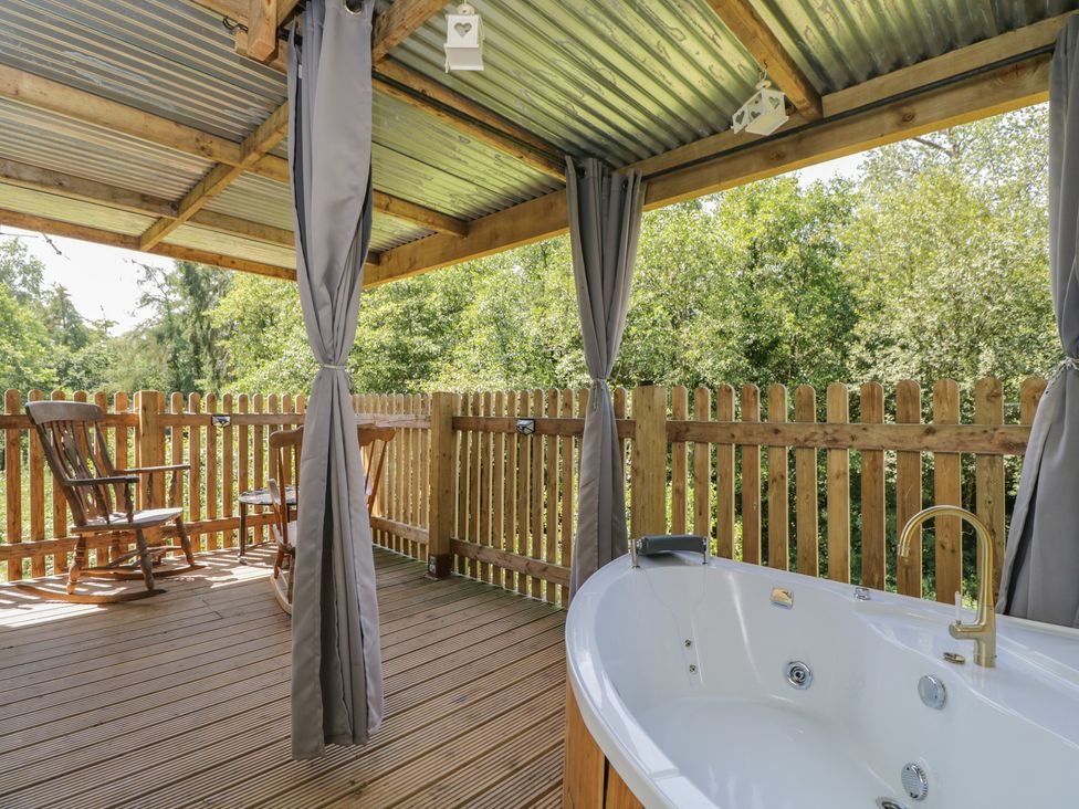 An outdoor patio with a hot tub and a rocking chair at Robins Nest Lodge in South Molton